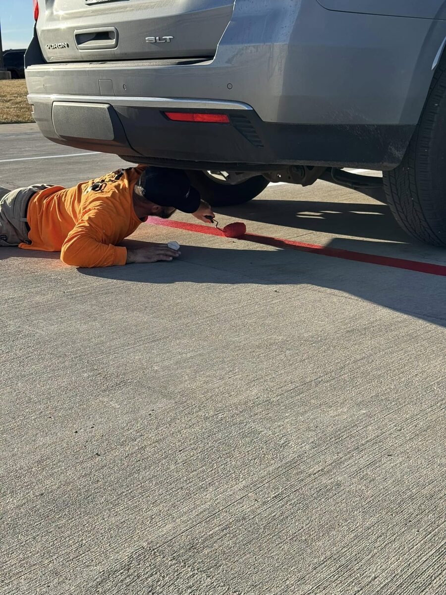 Worker hand-painting a red curb line in a parking lot